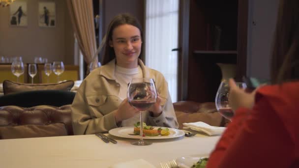 Dos novias positivas sentadas en el restaurante moderno, juntas. Las mujeres modernas toman fotos de su comida en el restaurante de lujo. Amigos tienen reunión en lugar cómodo — Vídeos de Stock