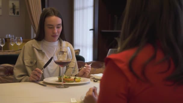 Duas namoradas bonitas sentadas no restaurante moderno, juntas. Meninas degustação de novo prato no restaurante de luxo. Amigos têm reunião no lugar confortável — Vídeo de Stock