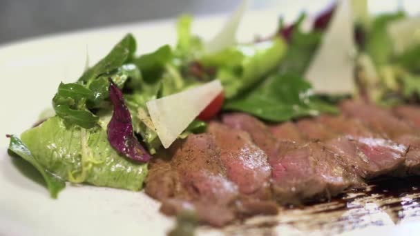 A salada fica perto do pedaço de carne crua marinada no prato de perto. Servindo a comida no restaurante moderno. Estilo de vida saudável. Câmera move à esquerda — Vídeo de Stock