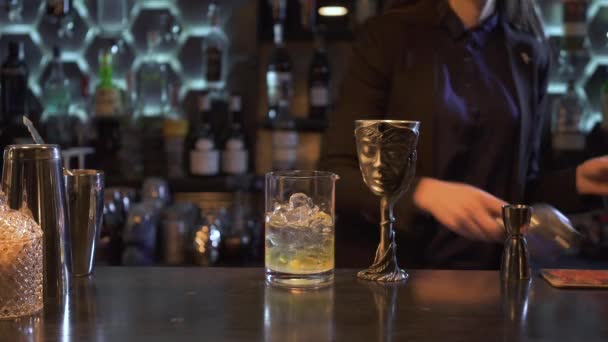 Barman girl avec de longs cheveux bruns presser le jus de citron à l'intérieur d'un cocktail avec de la glace dans un bol en verre et exclusif en métal sur le bar. Intérieur du restaurant incroyable — Video