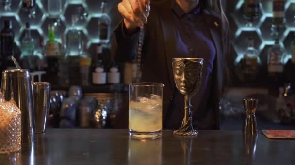 Wanita muda bartender cantik dengan rambut coklat panjang mencampur koktail dengan sendok panjang di kaca. Di bar adalah cangkir logam eksklusif dengan desain yang menakjubkan . — Stok Video