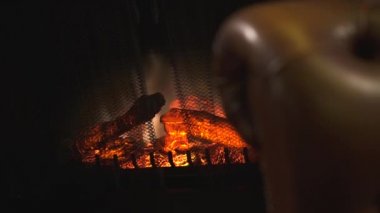 Elektrikli şömine kırmızı yapay parlak alev ve yanan kömürlerin bulanık kahverengi deri koltuk arka planda kapatın. Rahat bir yer, zengin ev veya modern lüks Restoran