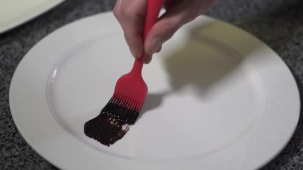 Ręce szefa kuchni stosowania grubych sause na płytkę za pomocą czerwonej gumy pędzla bliska w nowoczesnej restauracji. Kucharz, dekoracyjne płytki przed podaniem potrawy. Zwolnionym tempie — Wideo stockowe