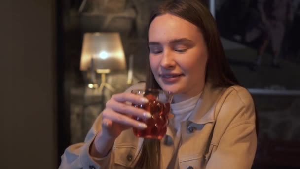 Mujer joven con el pelo castaño largo sentarse en el bar y beber bebidas en vidrio — Vídeo de stock