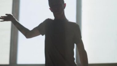 Genç tutkulu hip-hop dansçısı kamera önünde gerçekleştirme portresi kapatın. Adam kollarını ileri uzanır, sonra keskin kenarlara ile tüm vücut hareketleri yapar. Prova. Ağır çekim.