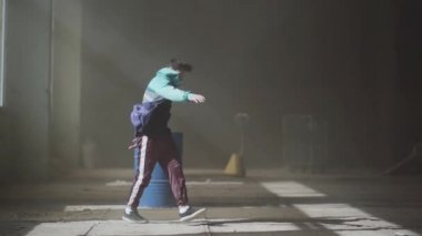 Genç Asyalı hip-hop erkek dansçı önünde mavi gaz varil bina terk karanlıkta dans spor giyim. Çağdaş. Hip hop kültürü. Prova. Ağır çekim.