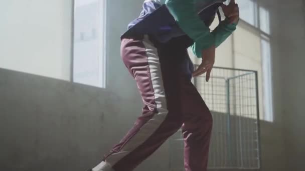 Joven bailarina callejera de hip-hop con experiencia actuando frente a una gran ventana en el oscuro edificio abandonado. El hombre haciendo movimientos, saltando y agachándose bailando.. Movimiento lento — Vídeo de stock