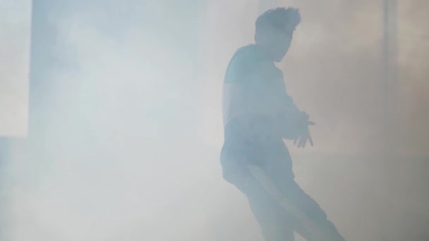 Молода азіатська хіп-хоп танцівниця, яка виступає в хмарі диму в покинутій будівлі. Чоловік робить ходи, стрибає і кружляє навколо. Повільний рух — стокове відео