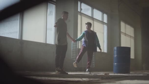 Two young men dancing in the dark and dusty room of abandoned building. Teenagers making dance move simultaneously, holding hands. Flexible men making wave with their bodies. Slow motion — Stock Video