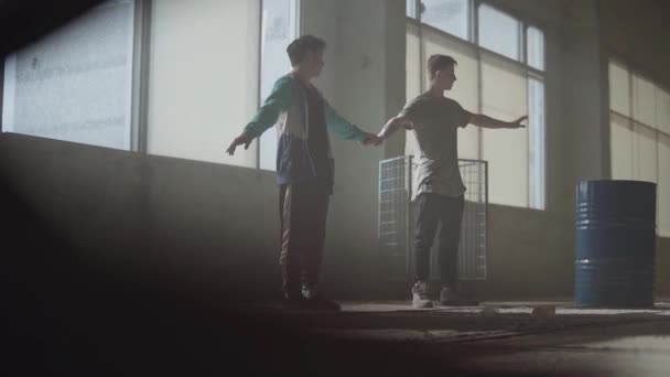 Dos hombres bailando en la oscura y polvorienta habitación del edificio abandonado. Adolescentes haciendo movimiento de baile simultáneamente, tomados de la mano. Hombres flexibles haciendo olas con sus cuerpos. Movimiento lento — Vídeos de Stock