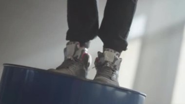 Hareket eder ve adımları gaz varil üzerinde yapma spor ayakkabı ayaklarda görünümünü kapatın. Genç hip hop erkek dansçı terk edilmiş binasında tozlu karanlık odada büyük pencerenin önünde gerçekleştirme.