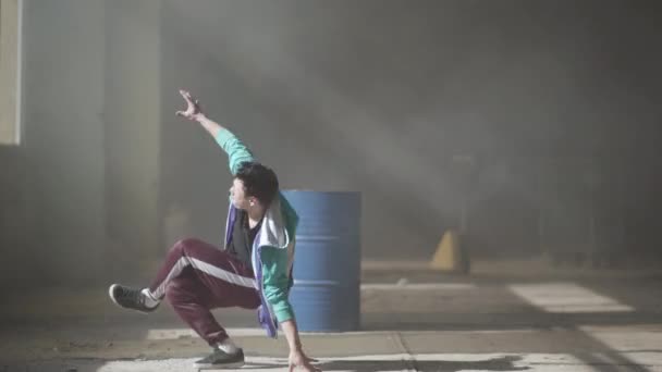 Досвідчений молодий хіп-хоп танцюрист танцює біля стволу в покинутій будівлі в тумані. Культура хіп-хопу. Репетиція. Сучасний . — стокове відео