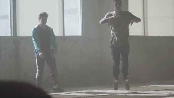 Dos chicos bailando frente a la gran ventana del edificio abandonado. Adolescentes haciendo movimiento de baile simultáneamente. Chicos practicando en breakdance. Cultura hip hop. Ensayo. Contemporáneo . — Vídeos de Stock
