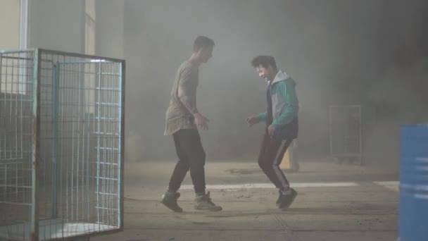 Dos jóvenes hábiles bailando en la oscura y polvorienta habitación del edificio abandonado. Los chicos haciendo movimientos de baile y poses. Amigos practicando en break-dance. Cultura hip hop. Ensayo. Contemporáneo . — Vídeo de stock