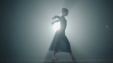 Siyah bir arka planda Spotlight stüdyosunda siyah elbise dans zarif sert çalışan balerin. Klasik balenin dans unsurlarını gerçekleştiren Diligent Bale dansçısı. Yavaş hareket.