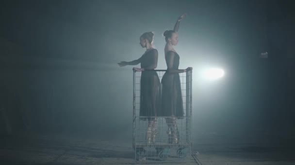 Dos elegantes bailarinas profesionales bailando en sus zapatillas de ballet puntiagudas en el centro de atención sobre fondo negro en el estudio. Bailarines de ballet muestran pasos clásicos de ballet de pie en un carro de metal . — Vídeos de Stock