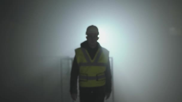 Portret van de ingenieur in de bouwers uniform en helm op een zwarte achtergrond in de kijker op de werkplek. — Stockvideo