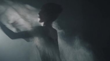 Genç balerin un atar ve stüdyoda siyah arka planda spot klasik bale unsurları gösterir.