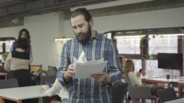 Ofiste ayakta kağıt belgeleri okuyan konsantre sakallı adam. Ofiste bisiklet sürme ve omzunda sakallı adam iter ve beş veren genç meslektaşım.