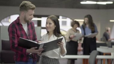 Ofis personeli, büyük kağıt klasör ile ofiste gelecekteki ayakta için raporlar ve planlar ile kağıtlar okuyor. Arka planda kadın meslektaşları ellerinde belgeler hakkında konuşuyor
