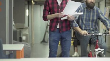 Sakallı ofis işçisi ofiste bisiklete biniyor. Bir adam iş yerinde evraklarla ayakta iş arkadaşı aşağı darbe ve raporlar ve gelecek için planlar ile belgeler okuyor. Işyeri.