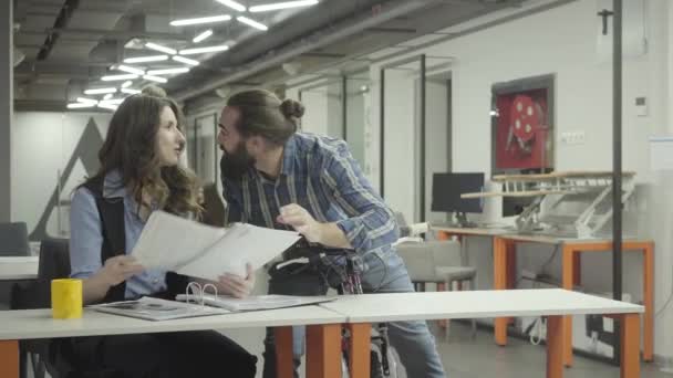 Mujer guapa y guapo barbudo se comunican en la oficina, riendo. Barbudo discutiendo emocionalmente información con una dama, sosteniendo su bicicleta. Colegas sonrientes y positivas. Lugar de trabajo . — Vídeos de Stock