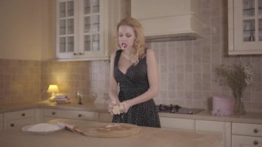 Siyah elbise büyük göğüsleri ile sarışın kadın mutfak masasında ağzına sigaret ile hamur yoğurun