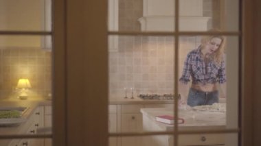 Genç ince sarışın çıplak göbek ile mutfak hamur yoğurma ve sonra masada oturmak ve bir kitap okumaya başlayın. Pencereden görüntüleme