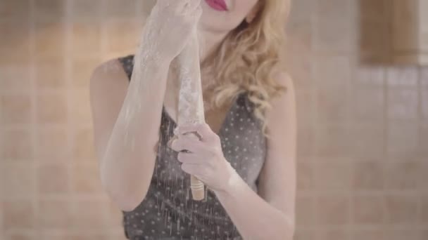 Gros plan portrait séduisante jeune femme blonde souriante avec rouge à lèvres et gros seins en robe noire frotte rouleau à pâtisserie avec de la farine. Passionnée fille préparer la pâte dans la cuisine à la maison . — Video