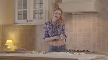 Bir şehvetli vücut ile portre baştan çıkarıcı kız mutfak masasında ayakta iken hamur hazırlar. Neşeli kız bir haddeleme pin ile hamur ve dans yoğurma.