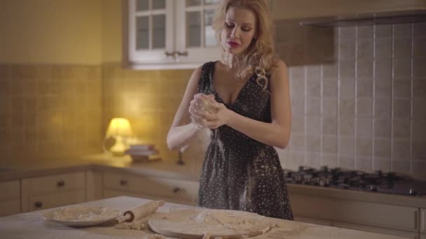 Jolie femme séduisante en robe noire enduite de farine mélangeant la pâte dans les mains et jette avec force la pâte dans la farine couchée sur la table de cuisine. La farine se disperse. Mouvement lent . — Video