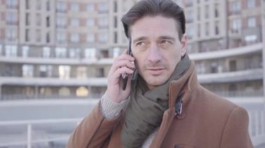 Cep telefonu ile konuşan şehir caddesinde kahverengi ceket ayakta yakışıklı emin adam portre. Arka planda kentsel şehir manzarası. Modern şehir sakinler