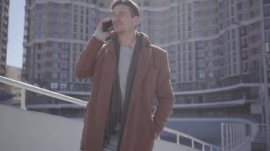 Şehir sokakta cep telefonu ile konuşan kahverengi ceket ayakta yakışıklı emin adam. Genç Blong kadın gelir ve adamın gözlerini kapsar. Arka planda kentsel şehir manzarası. Mutlu çift bir tarih var