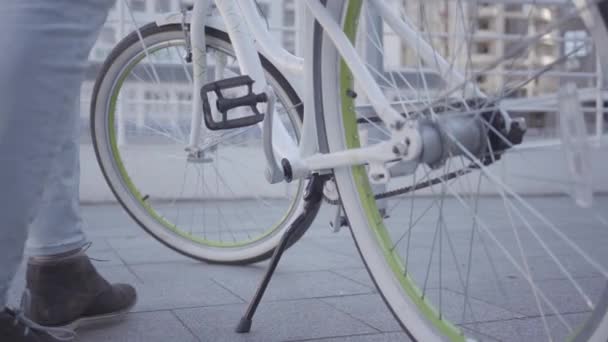Ноги молодого чоловіка, який сидить на велосипеді і їздить на ньому в місті крупним планом. Міський міський пейзаж на задньому плані. Дозвілля мешканця міста чоловічої статі. Активний спосіб життя — стокове відео