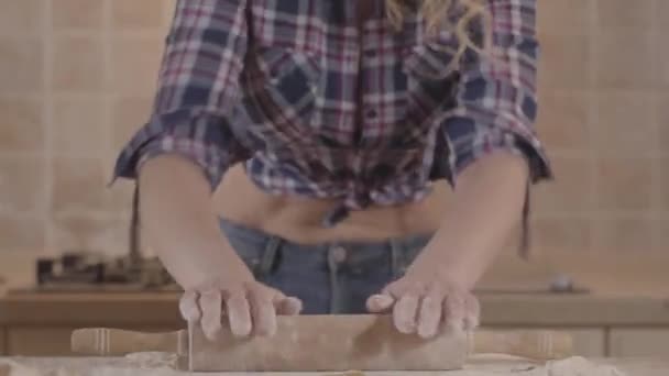 Fille passionnée avec un corps sensuel roule la pâte avec un rouleau à pâtisserie tout en se tenant à la table de la cuisine. Séduisante fille dans une chemise à carreaux avec un ventre nu . — Video