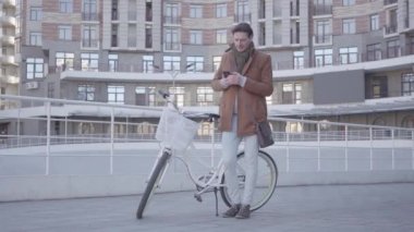 Kentsel mimarinin arka planına karşı bir bisiklet ile ayakta iken bir hücreye yazarak yakışıklı bir adamın portresi. Adam iyi güneşli havalarda açık havada dinleniyor.