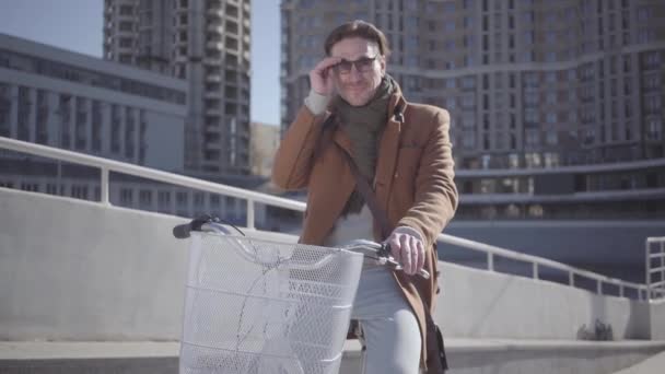 Portret van een jonge knappe man zittend op de fiets en het aantrekken van zonnebrillen. Leuke vent rusten tijdens het rijden een fiets buitenshuis. Fietsen. — Stockvideo