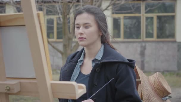 Portret geschoolde succesvolle kunstenaar verven op de ezel in de achtertuin. Mooi enthousiast meisje dat zich bezighoudt met creativiteit. Inspiratie. Talent. Kunstacademie of tekenschool. — Stockvideo