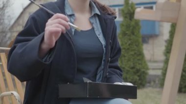 Genç bir kadın, arka bahçede atmosferik bir atölyede, bir bahçesinin arkasında duran bir tuval üzerinde bir resim boyar. Ilham. Yetenek. Sanat Akademisi veya çizim Okulu.