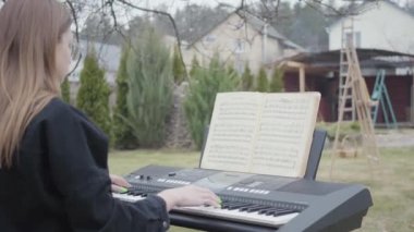 Profesyonel sevimli piyanist arka bahçede synthesizer klasik piyano müziği oynamak. Gerçek insanlar serisi.