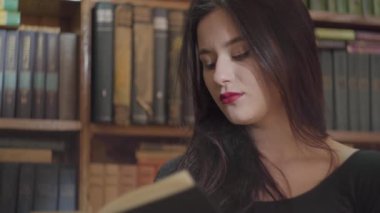 Kitaplık önünde duran bir kütüphanede bir kitap okuma parlak makyaj ile ciddi bir genç öğrencinin portre yakın. Akıllı çekici kadın Leisure.