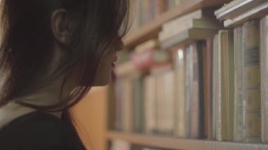 Kütüphanedeki kitabı seçen genç öğrencinin yan görünümü yakın. Kız kitap rafından eski kitabı alır. Akıllı çekici kadın Leisure