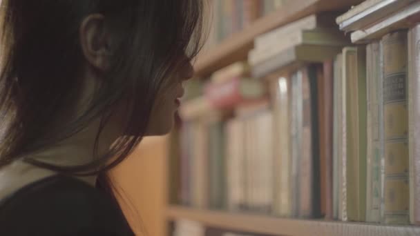 Vista lateral de la joven estudiante eligiendo el libro en una biblioteca de cerca. La chica toma el libro viejo de la estantería. Ocio de mujer atractiva inteligente — Vídeos de Stock