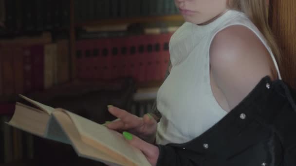 Mujer joven no reconocida leyendo un libro en una biblioteca de pie frente a la estantería. Ocio de mujer atractiva inteligente . — Vídeo de stock