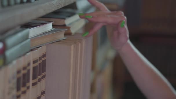 La mano femenina selecciona un libro en la estantería de la biblioteca. De cerca. . — Vídeos de Stock