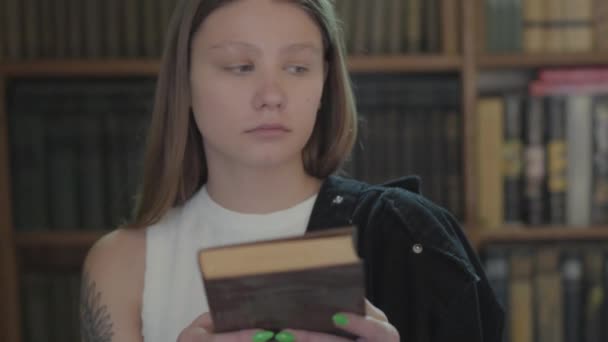 Portrait de la jeune fille mignonne étudiant mettant le livre sur la bibliothèque d’une librairie près. La fille passe son temps dans la librairie. Loisir de femme attirante intelligente — Video