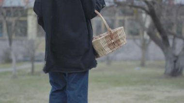 Genç kadının geri görünümü el fırça tutarak ceviz hasır sepeti ile yürüyüş. Kloş pantolon ve uzun gömlek çekici sanatçı bahçede topuklar üzerinde yürüyor. Country kız Leisure