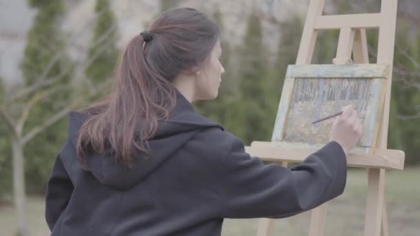 Successful artist paints on the canvas in the backyard. Beautiful enthusiastic girl engaged in creativity. Art academy or drawing school. Inspiration. Talent. — Stock Video