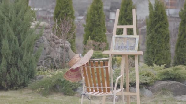 Back View van de lange jonge meisje schilder komt en zit in de voorkant van houten ezel om een foto te tekenen. Dame is roken. Vrouwelijke kunstenaar in Casual closing besteedt tijd buitenshuis, afbeelden landschap — Stockvideo