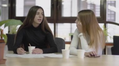 Bir mola sırasında modern bir iş ofisinde bir masada otururken iki meslektaşları sohbet ve kahve içme. İş yeri konsepti.